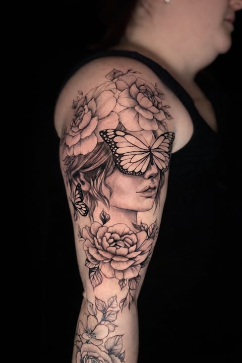 Black and gray tattoo sleeve featuring a womans profile with butterfly eyes and peony flowers covering the arm