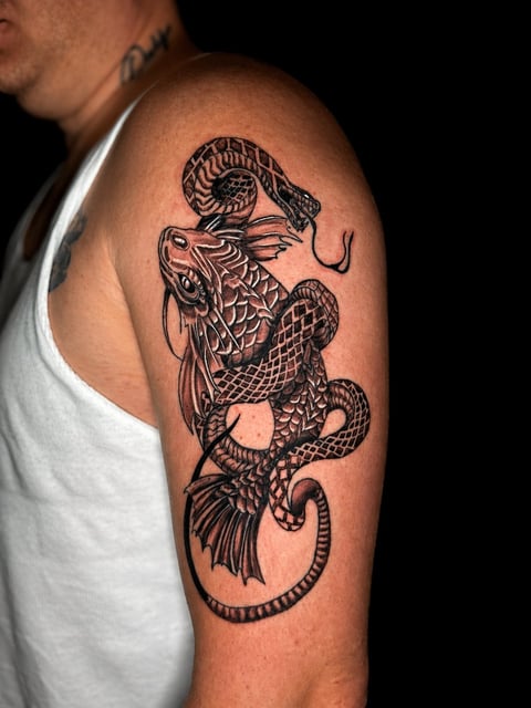 Black and red dragon tattoo wrapped around a mans upper arm on a black background