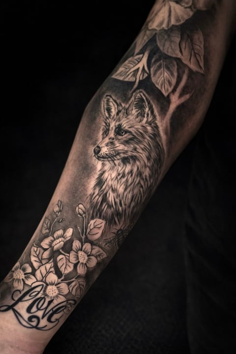 Arm tattoo sleeve featuring a fox head surrounded by leaves at the top and flowers at the bottom on black background