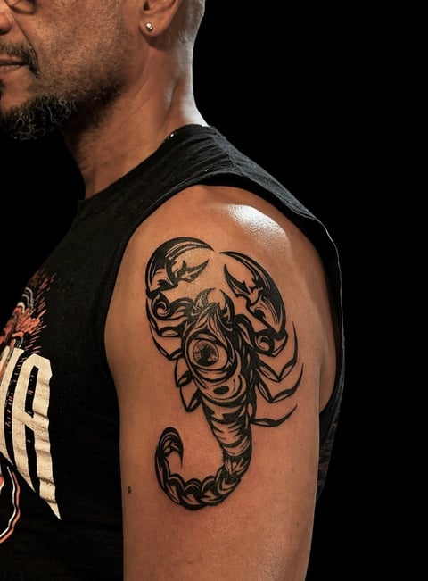 Mans upper arm with large black scorpion tattoo on shoulder against black background